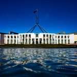 marcus-reubenstein-WWVLdFbTiVk-unsplash | LeapRate | Online Trading Industry News, Broker Intelligence & Fintech Analysis Front view of Parliament House Canberra with central flagpole and spire, white columns, reflected in the water.