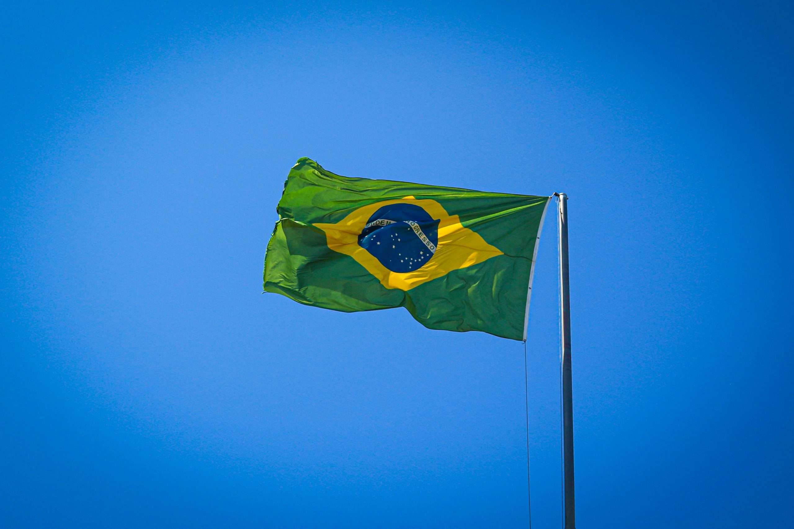 Brazilian flag fluttering on a flagpole against a clear blue sky