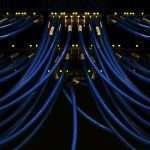 scott-rodgerson-PSpf_XgOM5w-unsplash | LeapRate | Online Trading Industry News, Broker Intelligence & Fintech Analysis Blue Ethernet/network cables run into a server rack, with yellow status LEDs glowing in the dark background.