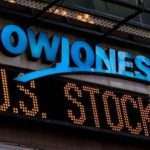 Dow Jones sign with a yellow-orange ticker display showing 'U.S. STOCKS' beneath a blue 'DOWJONES' logo.