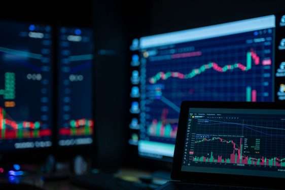 Trader monitoring multiple screens with stock market charts at a trading desk