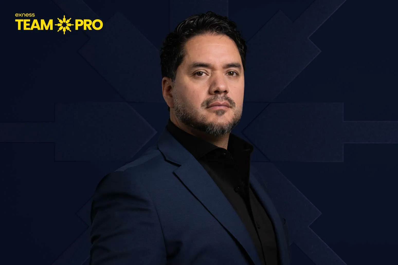Portrait of a man in a navy suit against a dark geometric background with the yellow Exness Team Pro logo in the top-left.