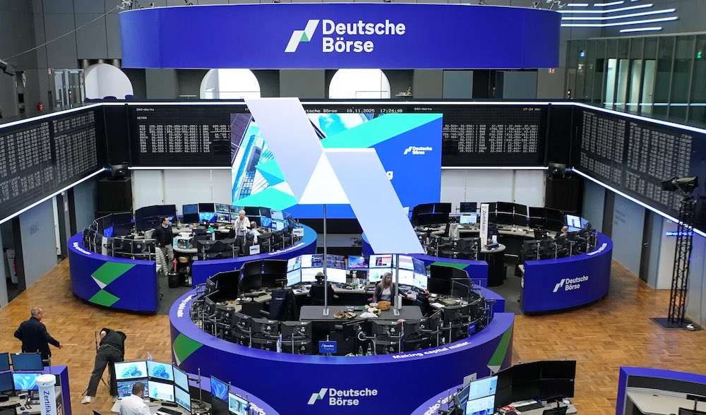 Deutsche-Börse | LeapRate Trading floor of Deutsche Börse with circular desks, multiple computer monitors, and a large blue Deutsche Börse sign overhead inside a modern, glass-walled atrium.